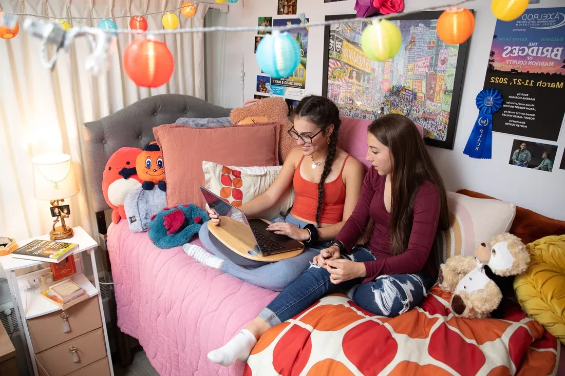 两个学生坐在床上，在宿舍里工作.